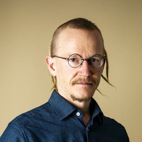 Portrait of Mikael Cromsjö, IT and AI consultant, in a blue shirt and round glasses