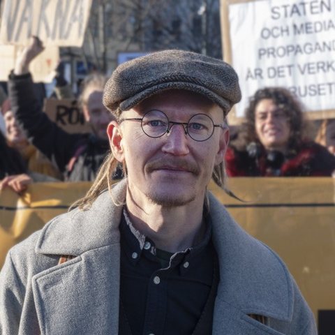 Mikael Cromsjö in a flat cap and round glasses at a freedom-movement demonstration in Sweden